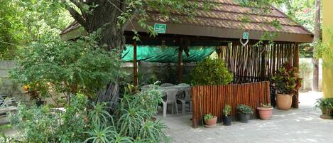 Relax in a serene outdoor space surrounded by lush greenery and potted plants, with a covered patio and comfortable seating for dining or relaxation.