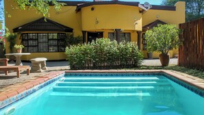 Un edificio amarillo con piscina, mobiliario de patio y plantas en macetas.