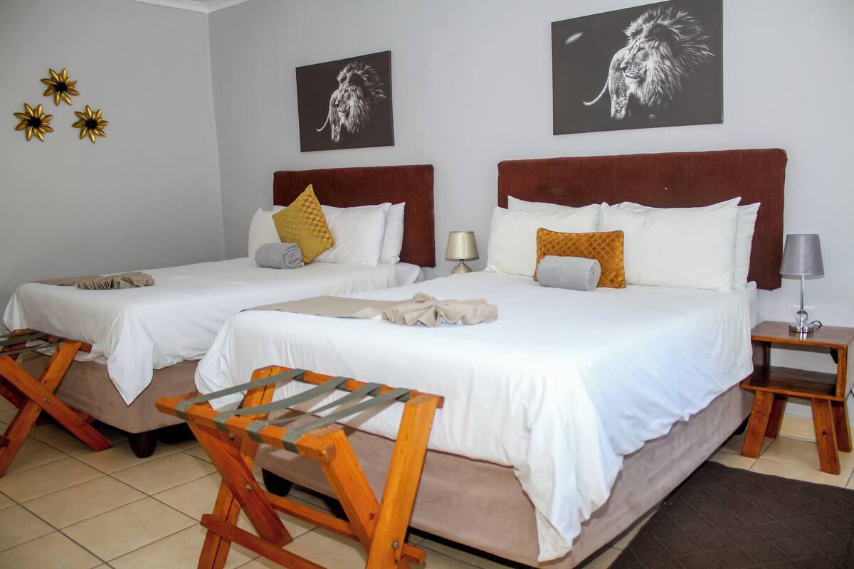 A double bed with white bedding and two pillows, a wooden chair, and a nightstand with a lamp.