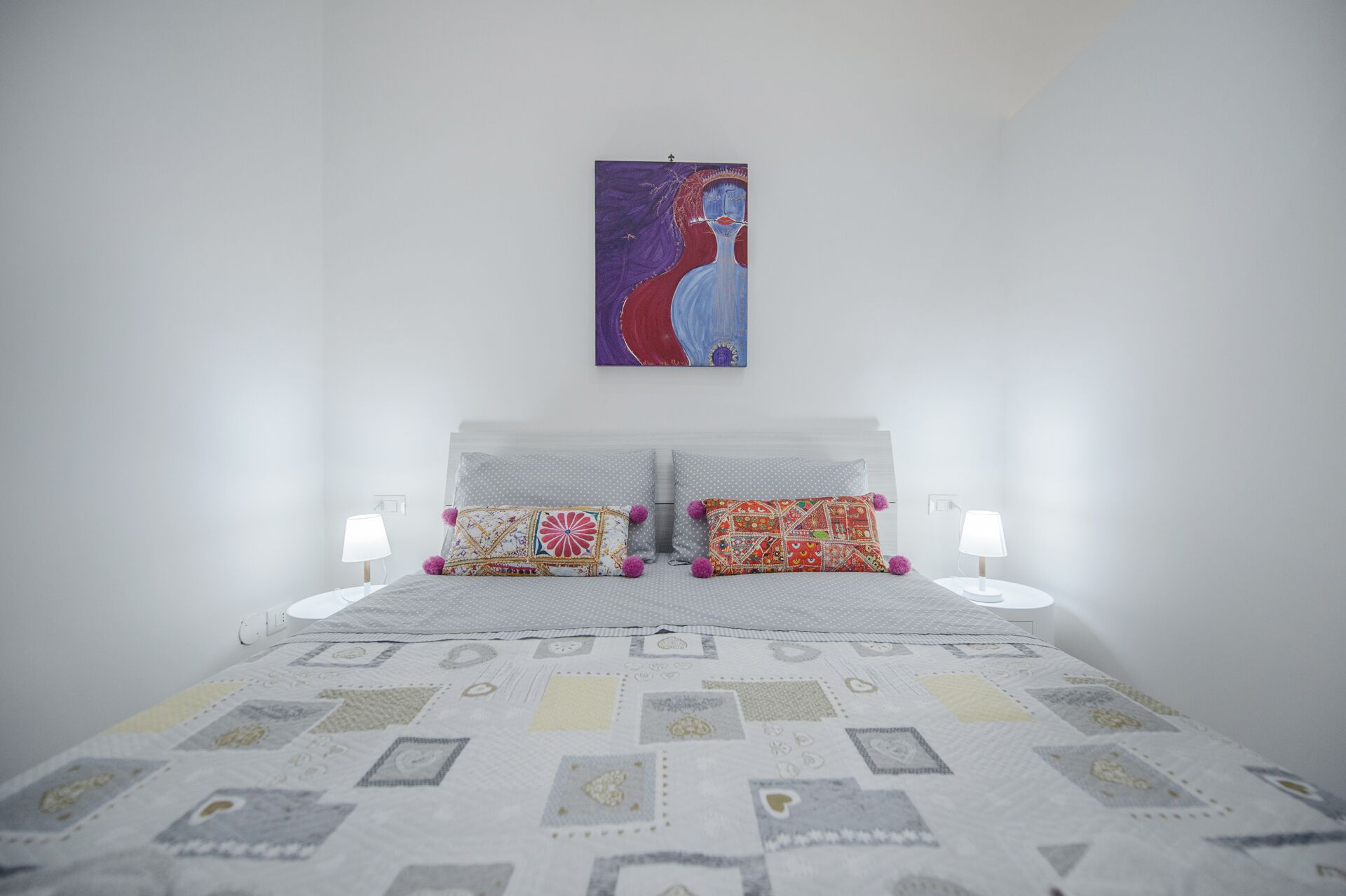Une chambre à coucher avec un lit, deux oreillers, deux lampes de chevet et un tableau au mur.