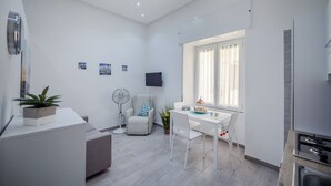 Un salon moderne et bien éclairé, comprenant un coin repas, un téléviseur à écran plat fixé au mur et une fenêtre avec des rideaux.