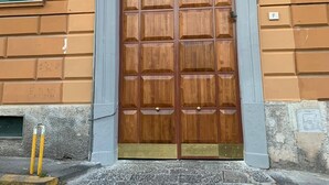 Une grande porte en bois ornée d’une grille métallique décorative et surmontée d’un emblème représentant une tête de lion.