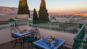 Una terraza con una mesa preparada para el desayuno, con vistas a un paisaje urbano y montañas al fondo.