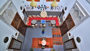 Vista del interior de un riad tradicional marroquí, con intrincados trabajos en azulejos, una zona de estar central con cojines y faroles colgantes.