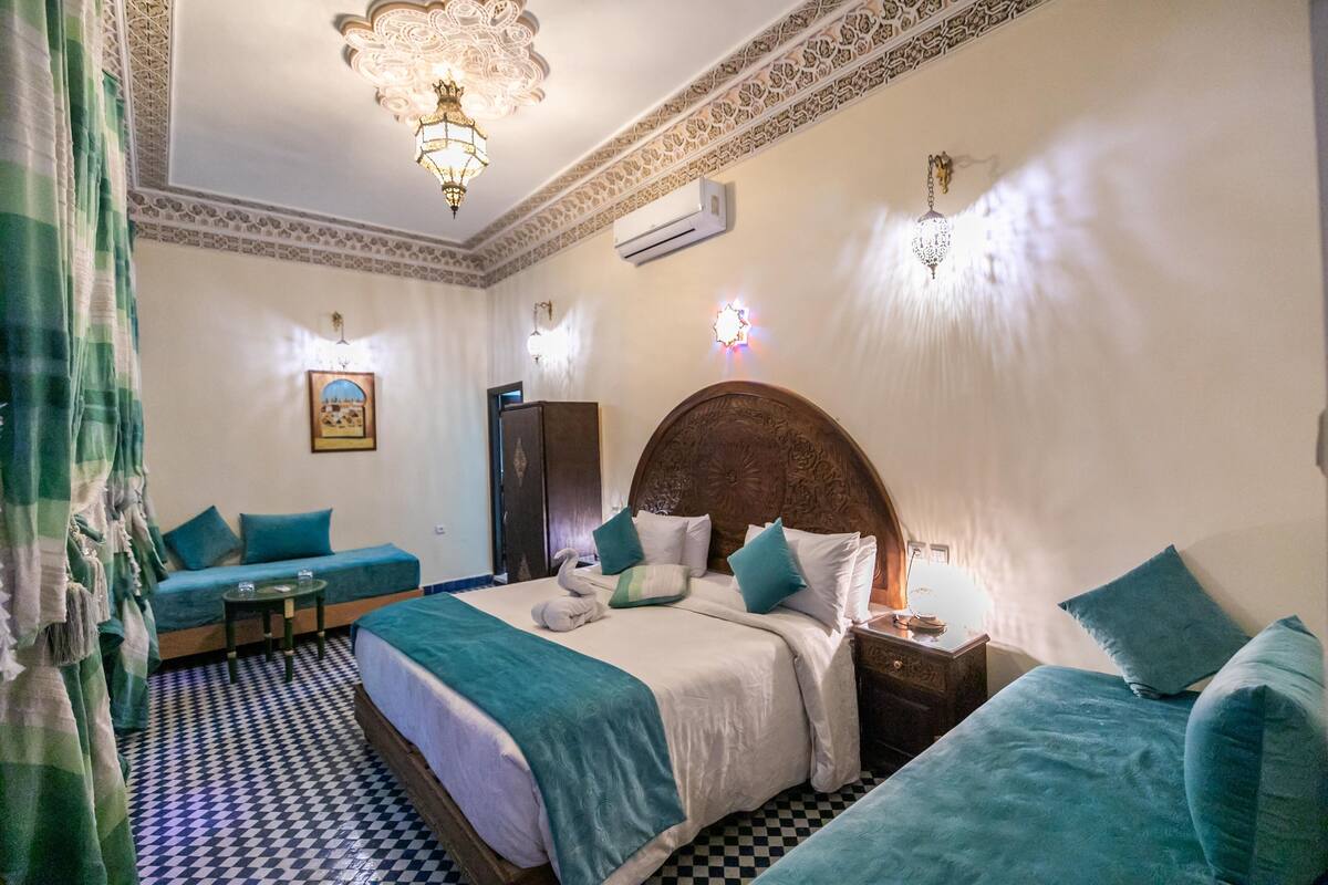 A hotel room with a large bed, a sofa, a small table, and a decorative ceiling light.