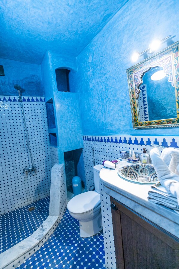 Ein Badezimmer mit blau-weißen Fliesen an Boden und Wänden, einer weißen Toilette, einem Waschbecken mit Verzierten Fliesen und einer Duschkabine.