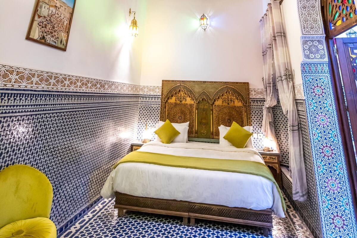 A room with a patterned ceiling, a bed with a headboard, a wall-mounted air conditioner, and a framed picture.