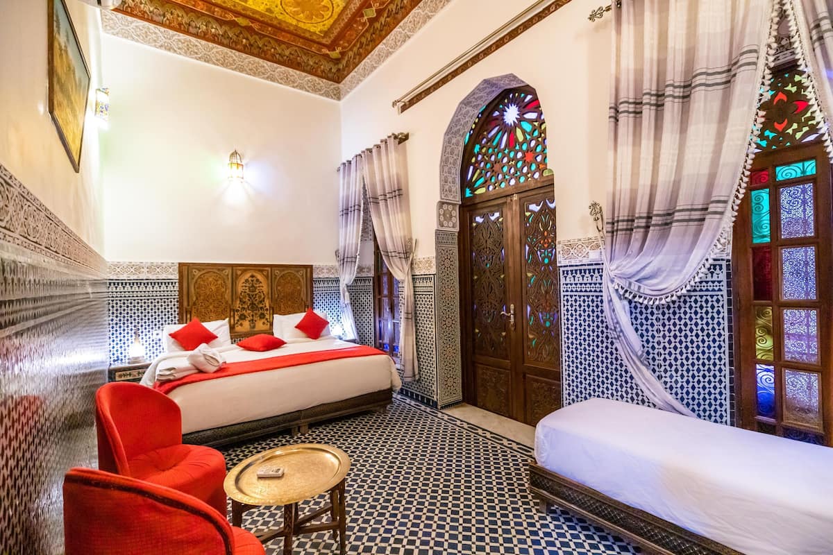 A room with a bed, red chairs, a small table, and a decorative door with intricate patterns.