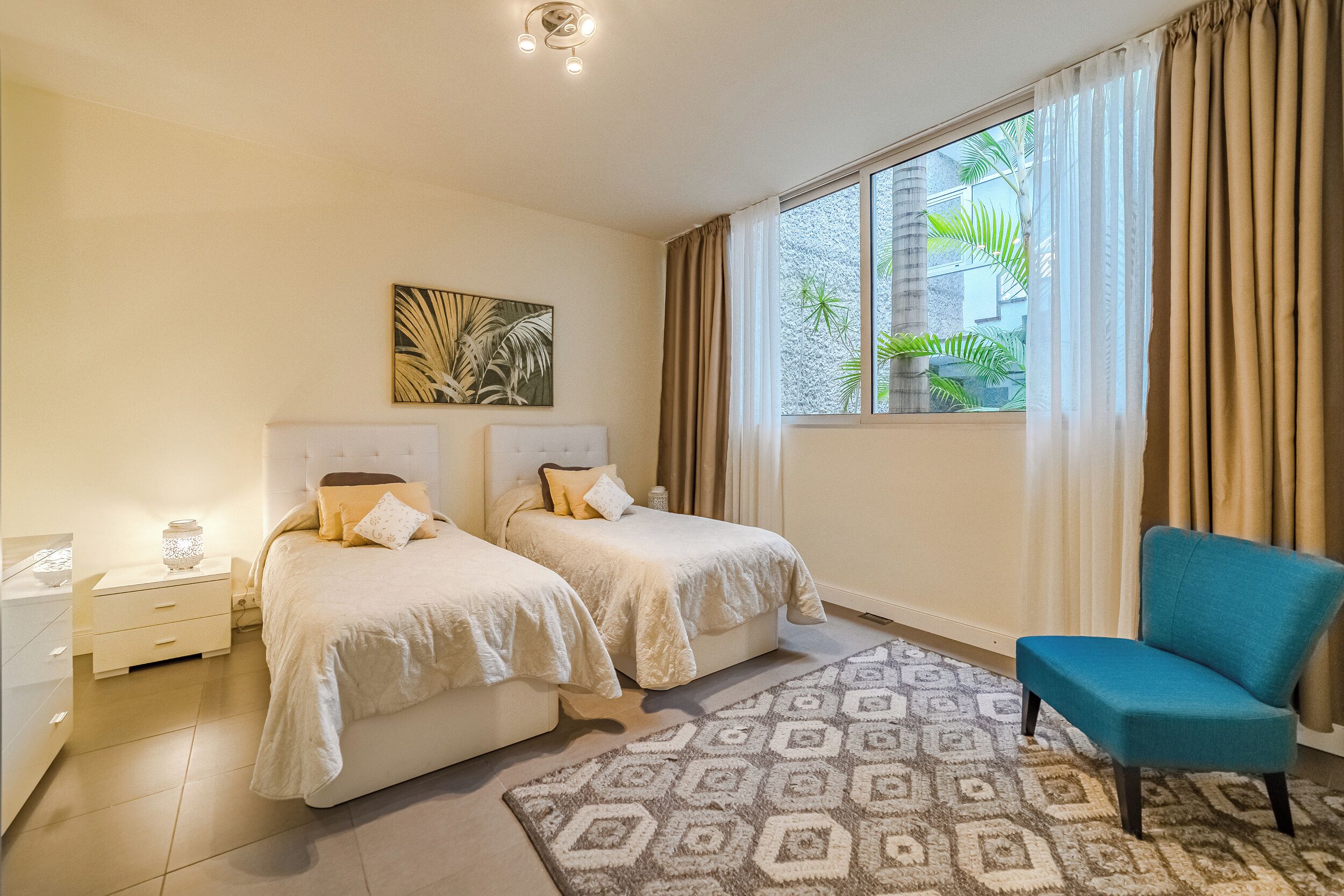 A hotel room with two beds, a nightstand, a chair, and a window with curtains.