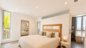 Ein Schlafzimmer mit einem großen Bett, einem Nachttisch, einem Spiegel und Blick ins Freie.