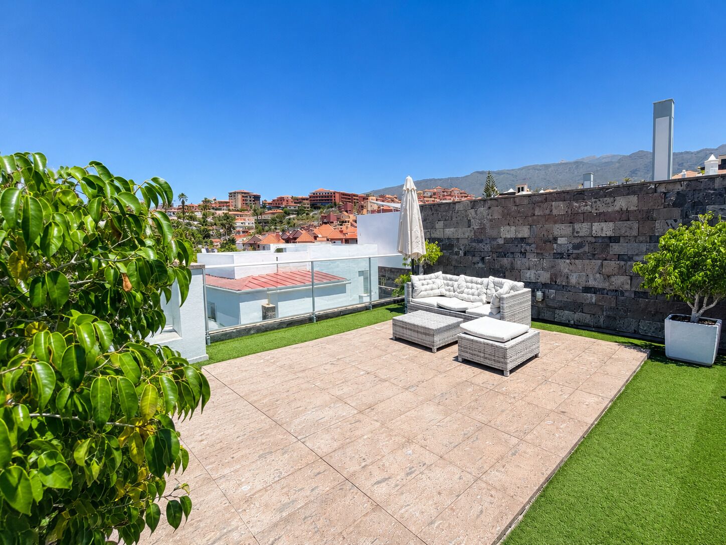 A rooftop patio with a white outdoor sofa, a small table, and a potted plant.