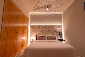 A bedroom with a large wooden wardrobe, a bed with a floral wallpaper headboard, and a modern ceiling light fixture. - Villa Guájara (Playa Blanca)