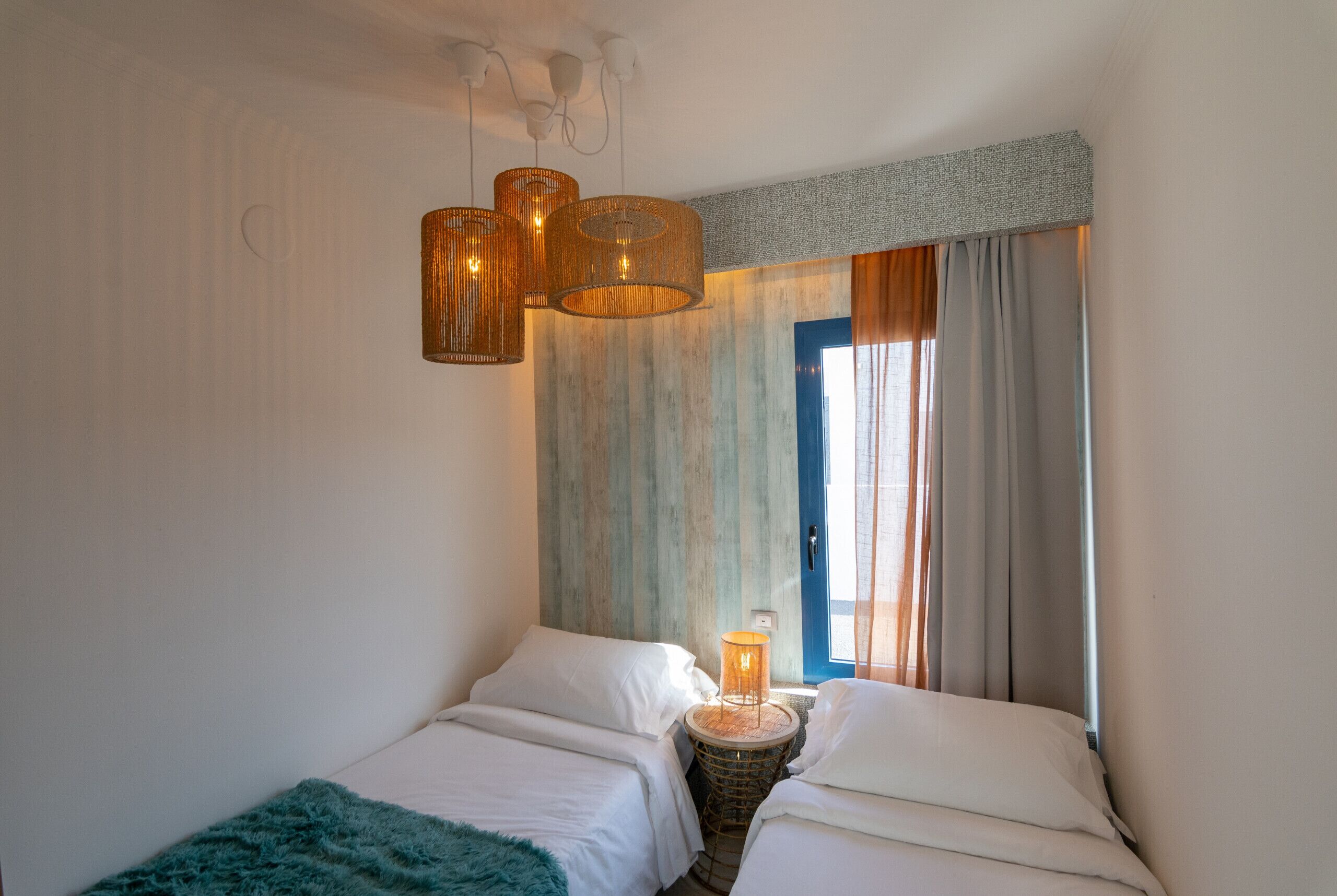 Une chambre avec deux lits, un luminaire en fibres tressées et une vue sur l’extérieur.