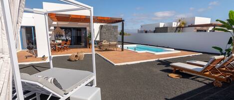 Un área de piscina moderna al aire libre con sillones de descanso, una zona de estar cubierta y una pared de piedra.