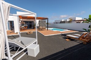 A modern outdoor pool area with lounge chairs, a covered seating area, and a stone wall. - Villa Guájara (Playa Blanca)