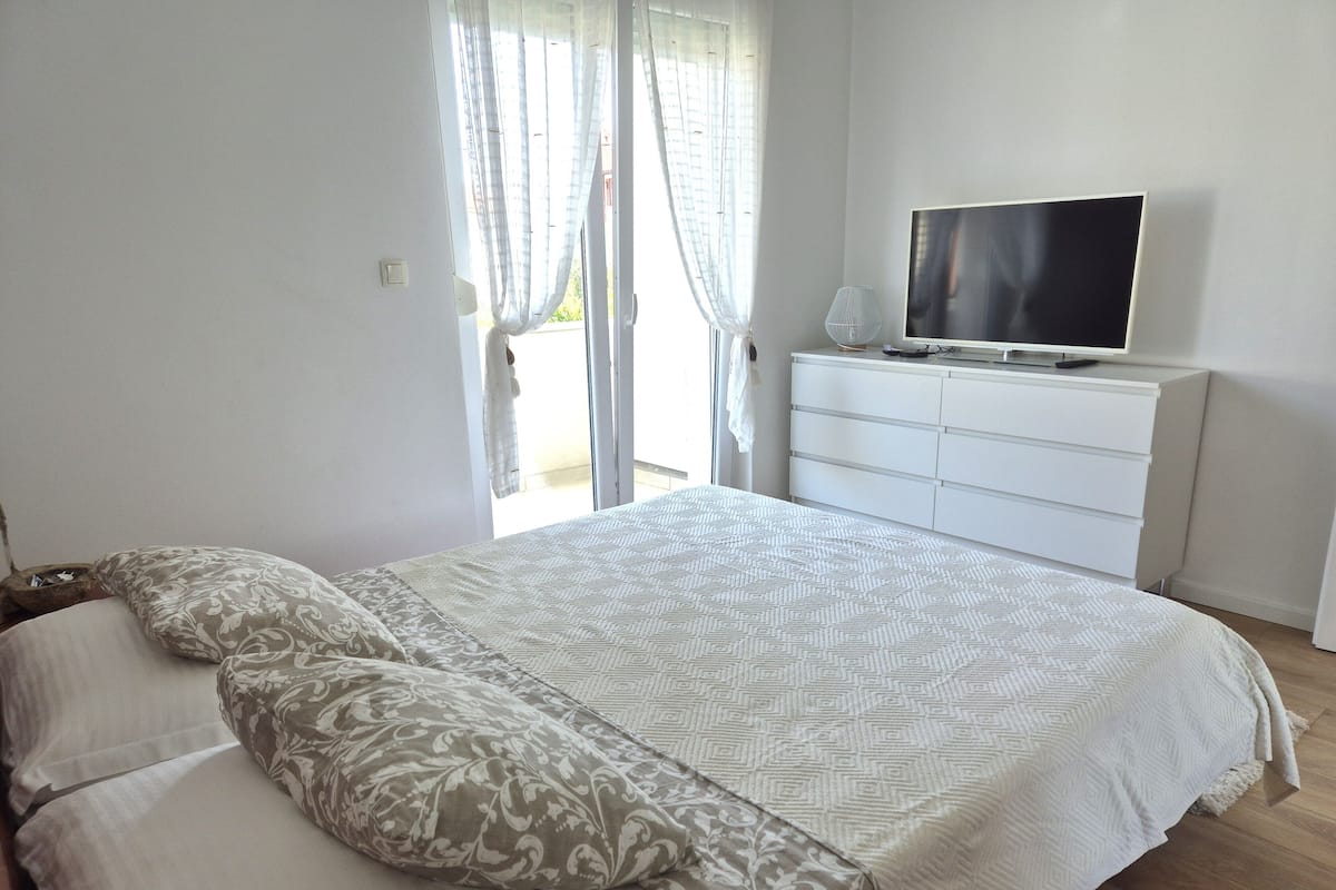 A bedroom with a bed, a television on a dresser, and a sliding glass door.