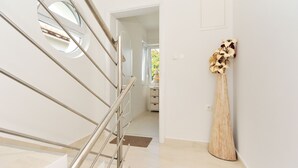 A modern interior with a staircase, a wooden vase with flowers, and a view through an open door. - Deluxe Apartments Goya (Zadar)