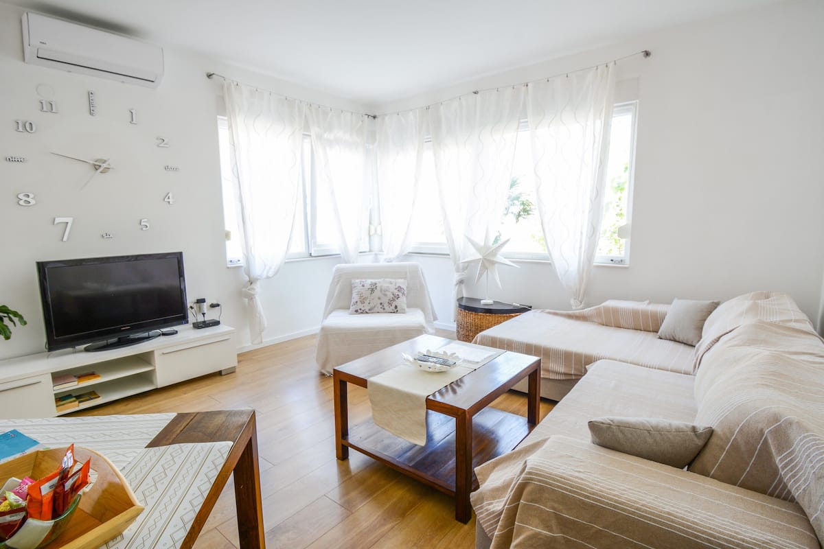 A modern living room with a flat-screen TV, a wooden coffee table, a beige sofa, and a white armchair.