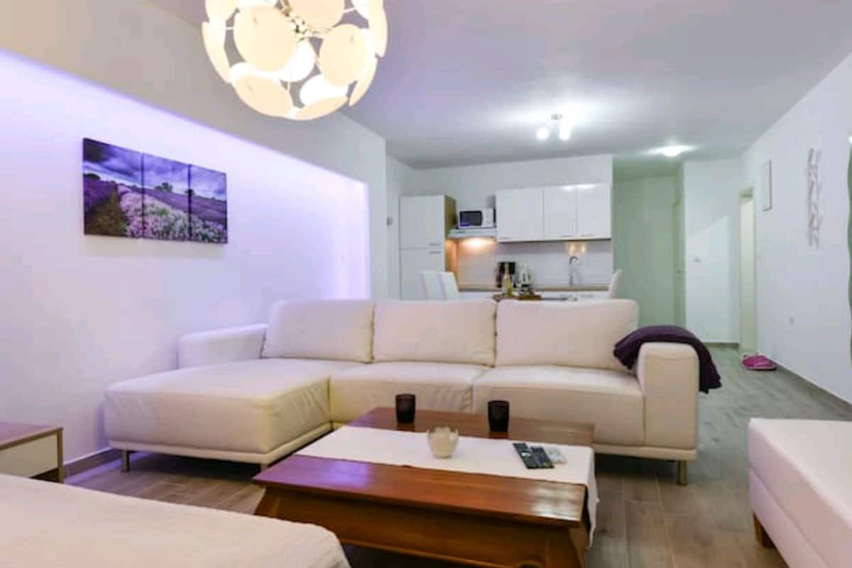 A modern living room with a sectional sofa, a wooden coffee table, and a kitchen area in the background.