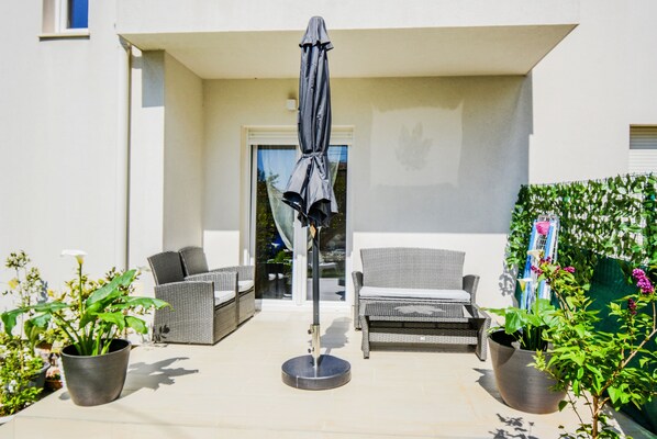 An outdoor patio area with wicker furniture, a round table, and a covered umbrella. - Deluxe Apartments Goya (Zadar)