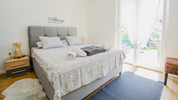 A bedroom with a bed, bedside tables, a nightstand, and a window with curtains. - Deluxe Apartments Goya (Zadar)