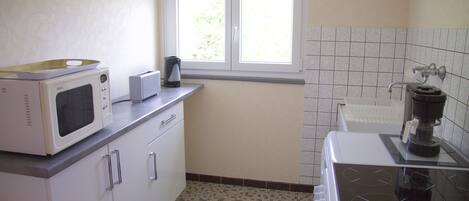 Cucina compatta con mobili bianchi, microonde, tostapane e macchina del caffè.