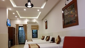 A hotel room with a large red sofa, two beds with white bedding and brown accents, a wooden coffee table, a TV on the left, and a painting on the wall. - Bean Grass Homestay (Da Nang)