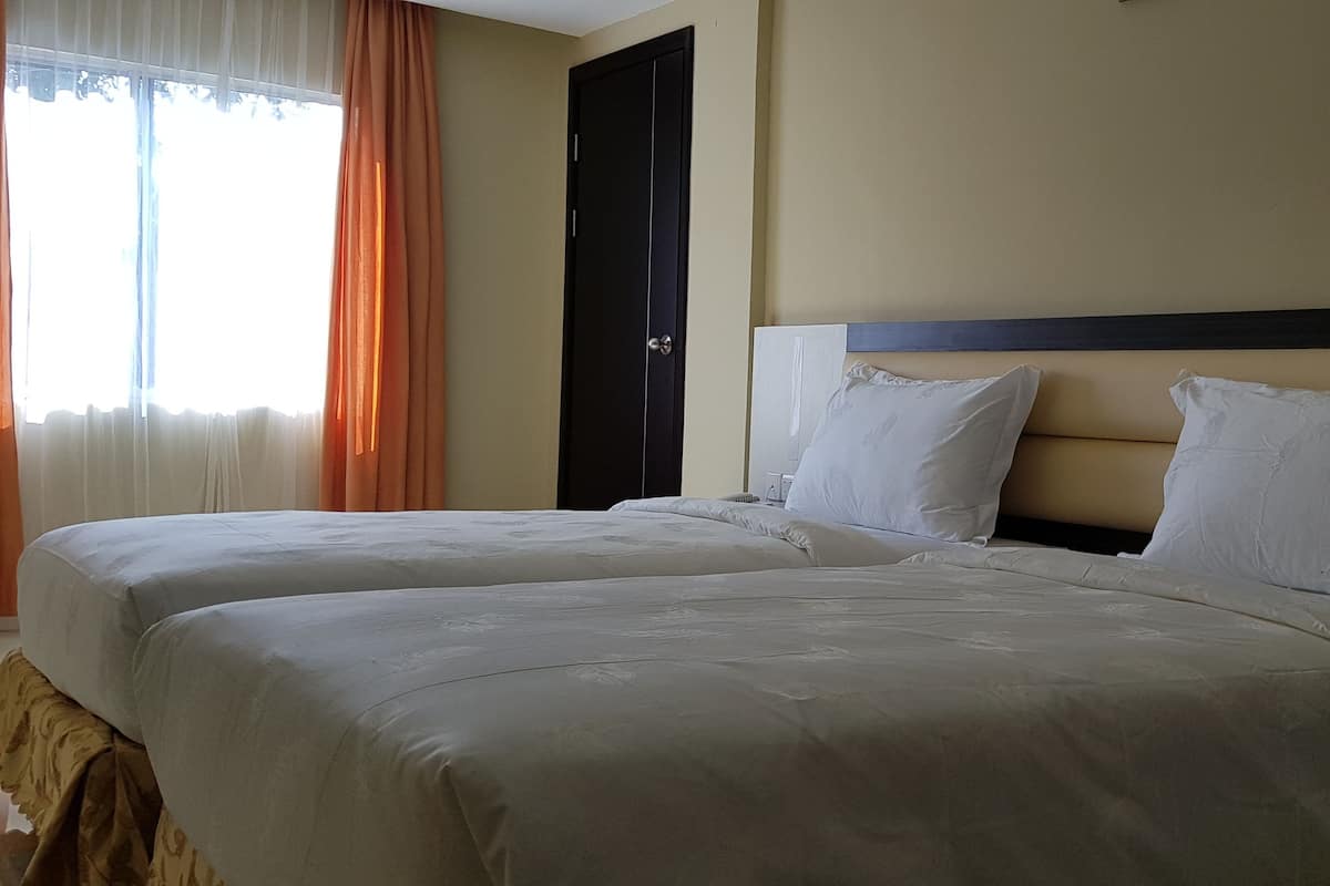 Habitación de hotel con dos camas, una silla de madera, una puerta oscura y una ventana con cortinas.
