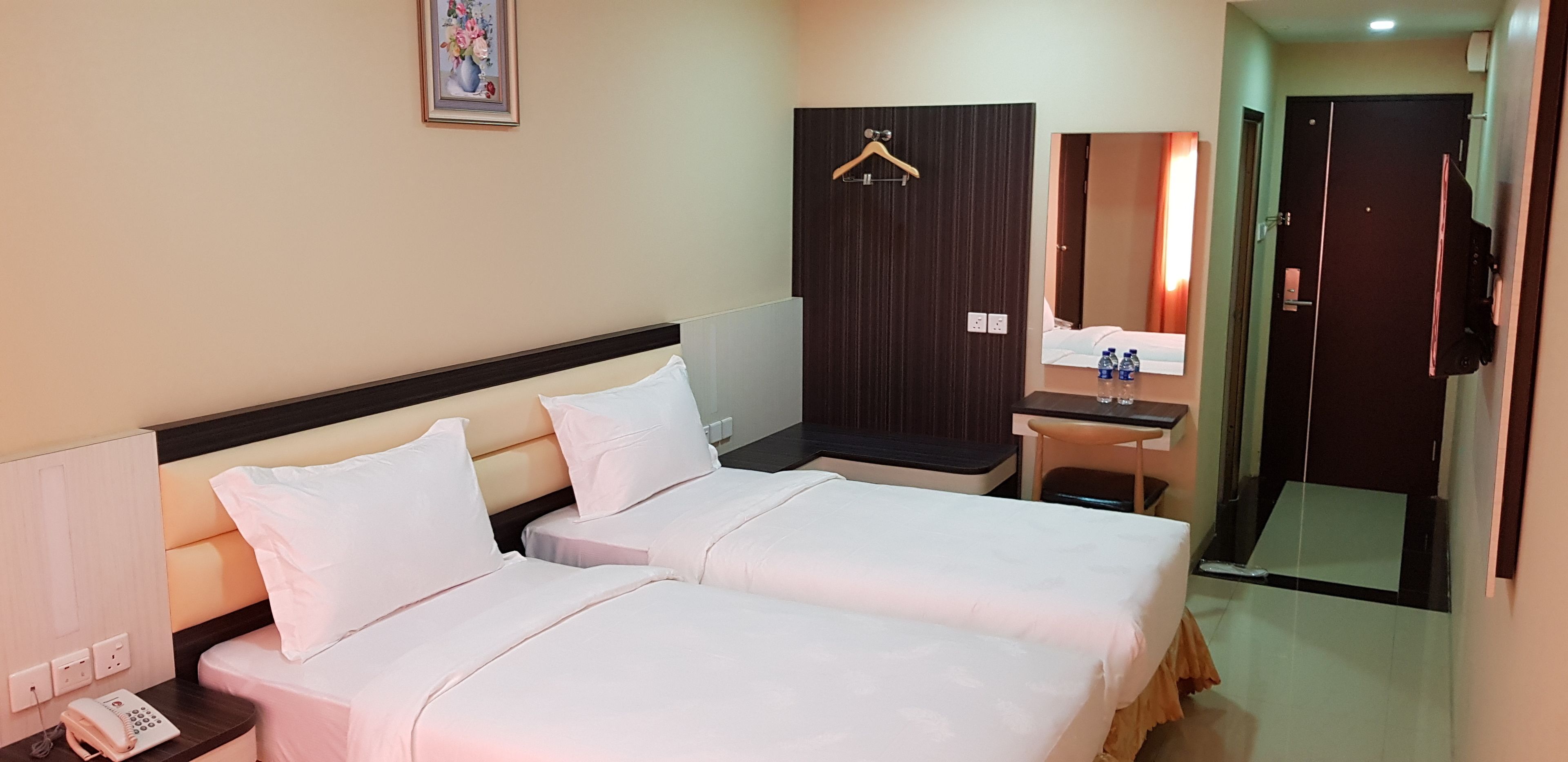 A hotel room with two beds, a desk, a mirror, and a door.