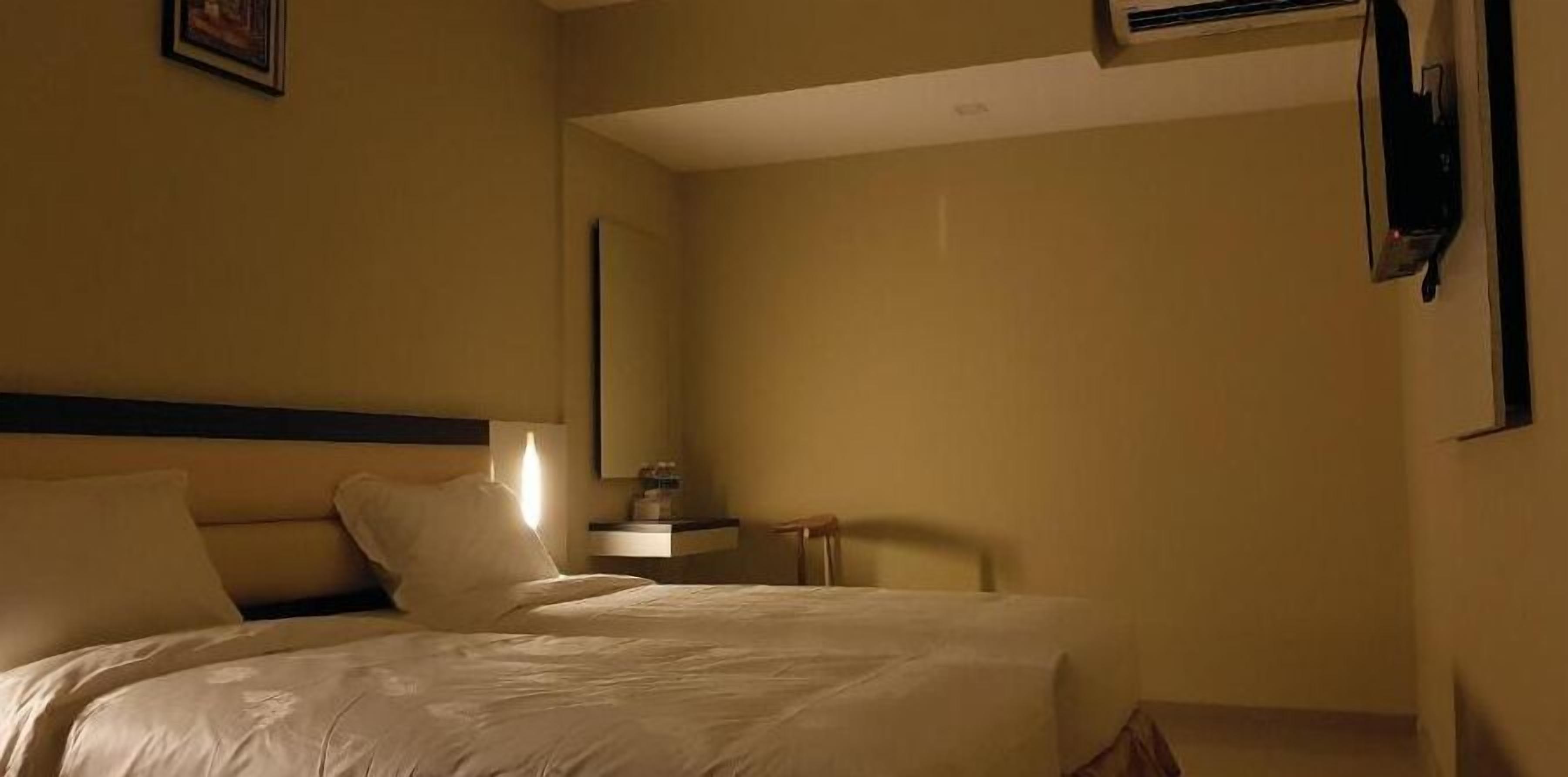 A hotel room with a large bed, a bedside table, a nightstand, and a mirror on the wall.