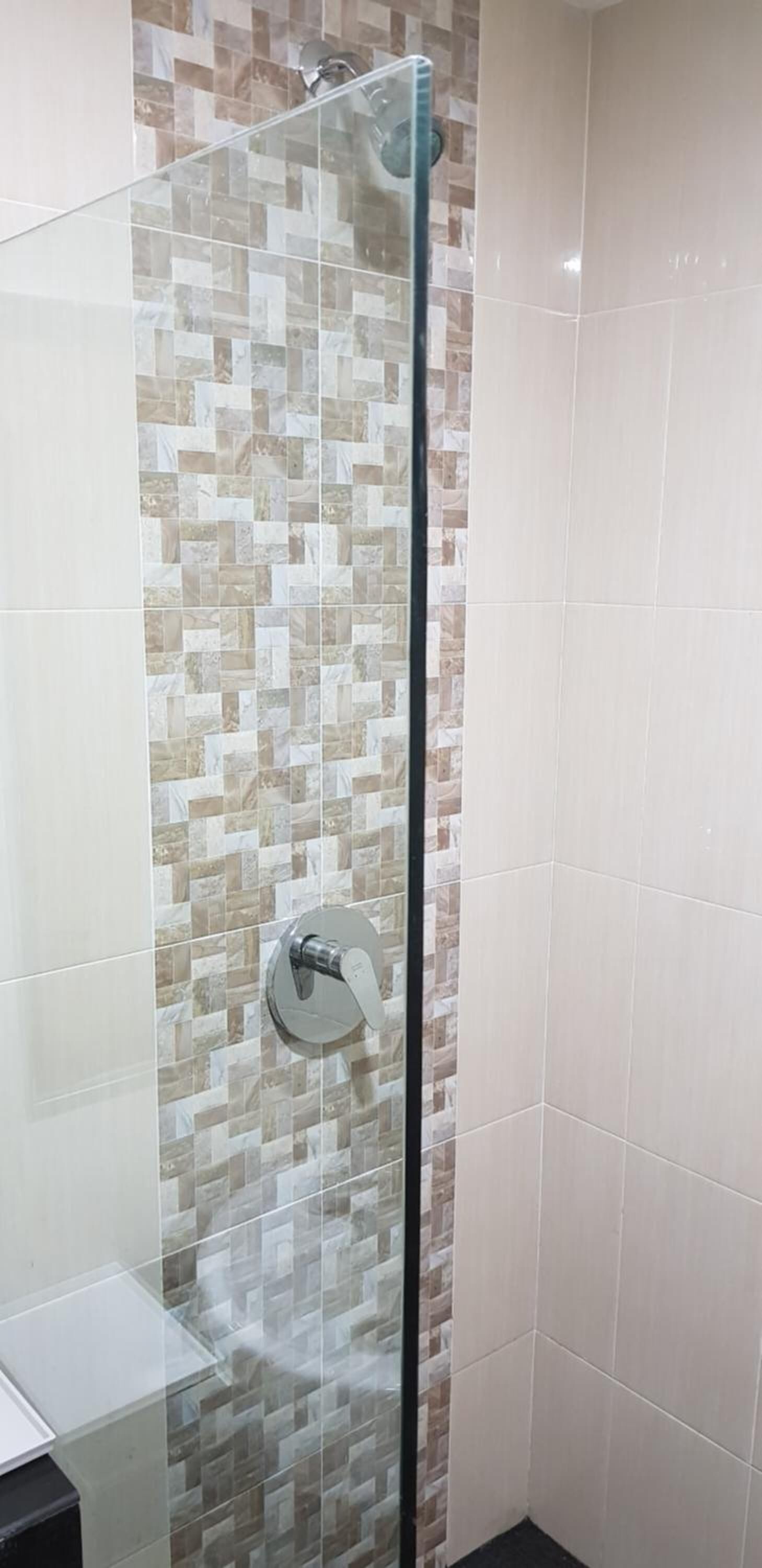 A glass-enclosed shower with a tiled wall featuring a mosaic pattern.