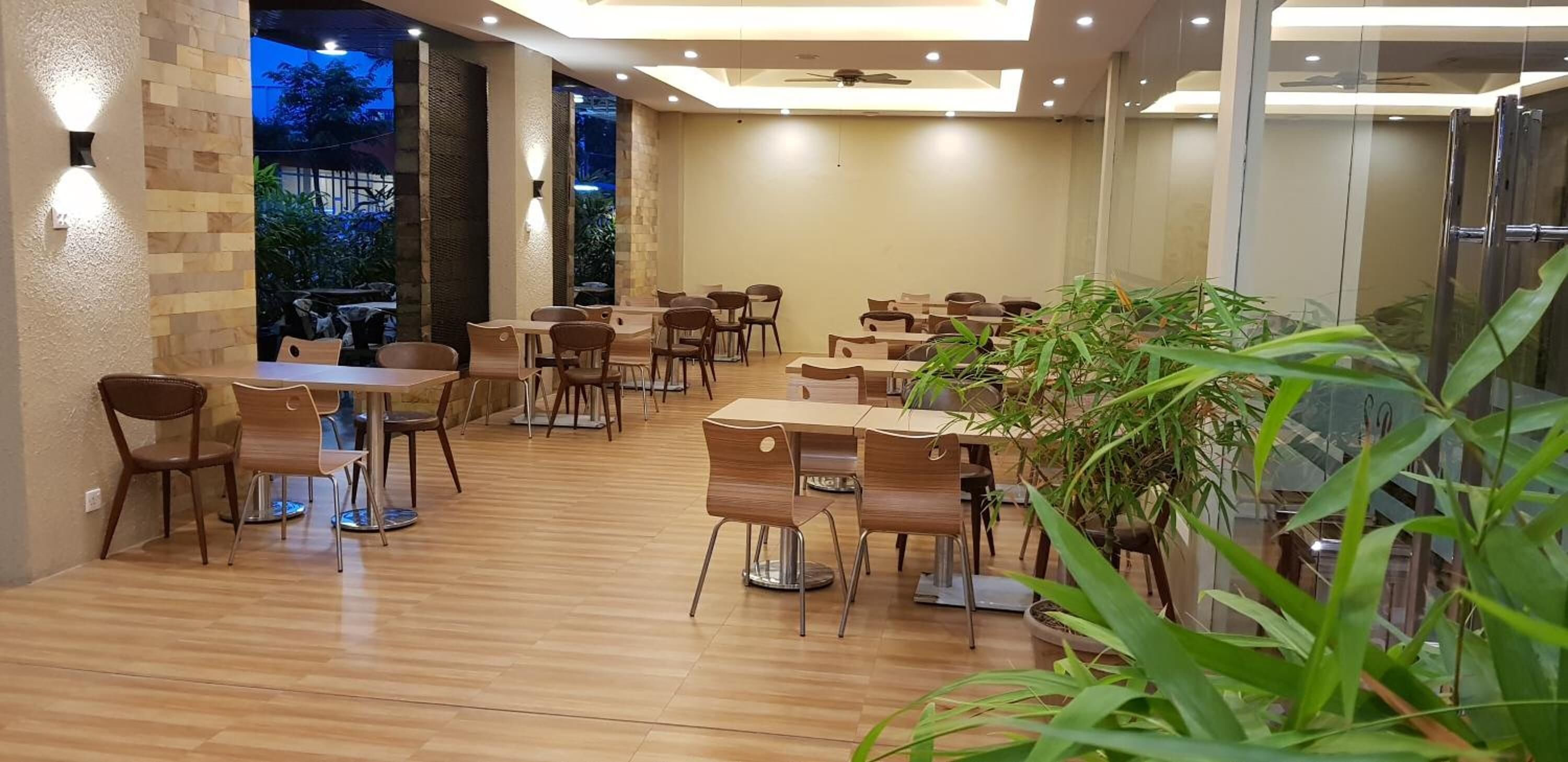 A spacious indoor dining area with wooden tables and chairs, a ceiling fan, and a view of the outdoors.
