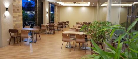 A spacious indoor dining area with wooden tables and chairs, a ceiling fan, and a view of the outdoors.