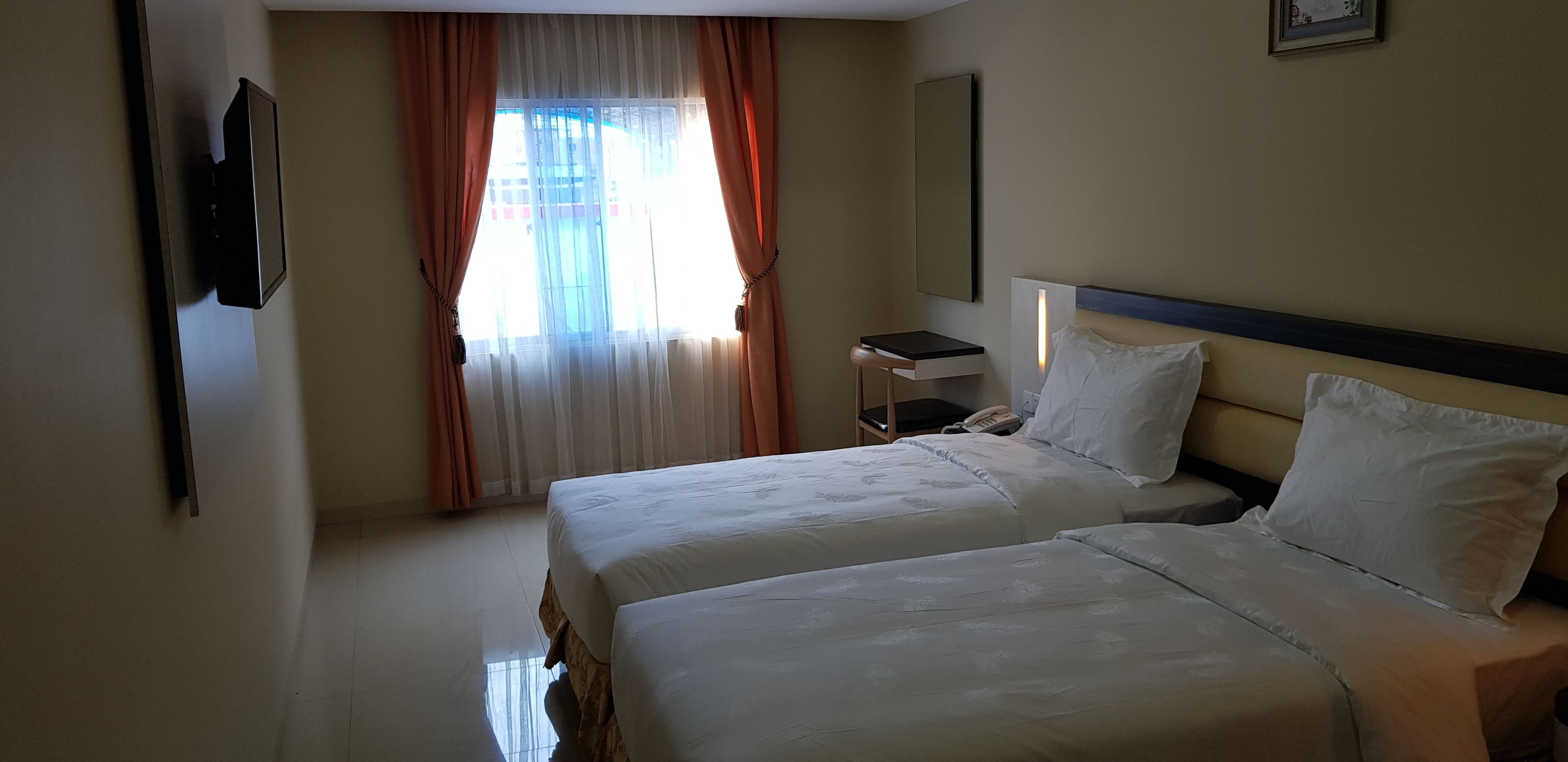 A hotel room with two beds, a desk, a phone, and a window with curtains.