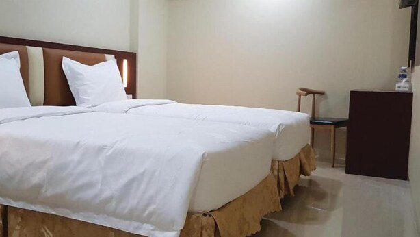 Una cama doble bien hecha con sábanas blancas, cabecero de madera y mesita de noche con lámpara.