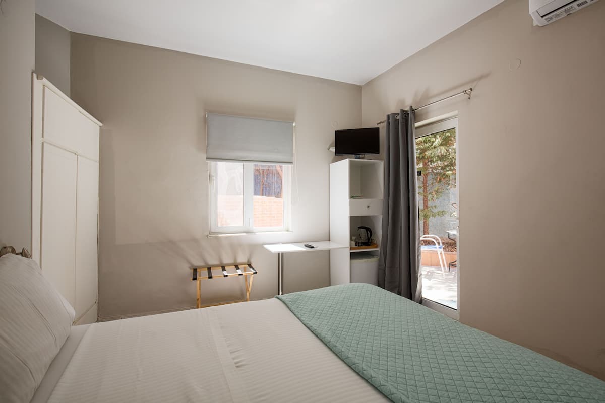 A bedroom with a bed, a desk, a chair, a TV, and a window.