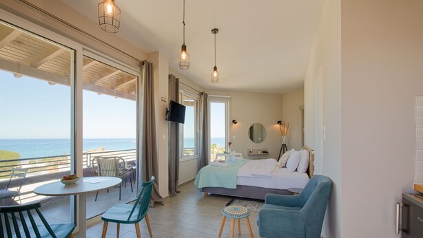 Habitación de hotel con balcón, una cama, un televisor y un área de comedor con sillas y una mesa.