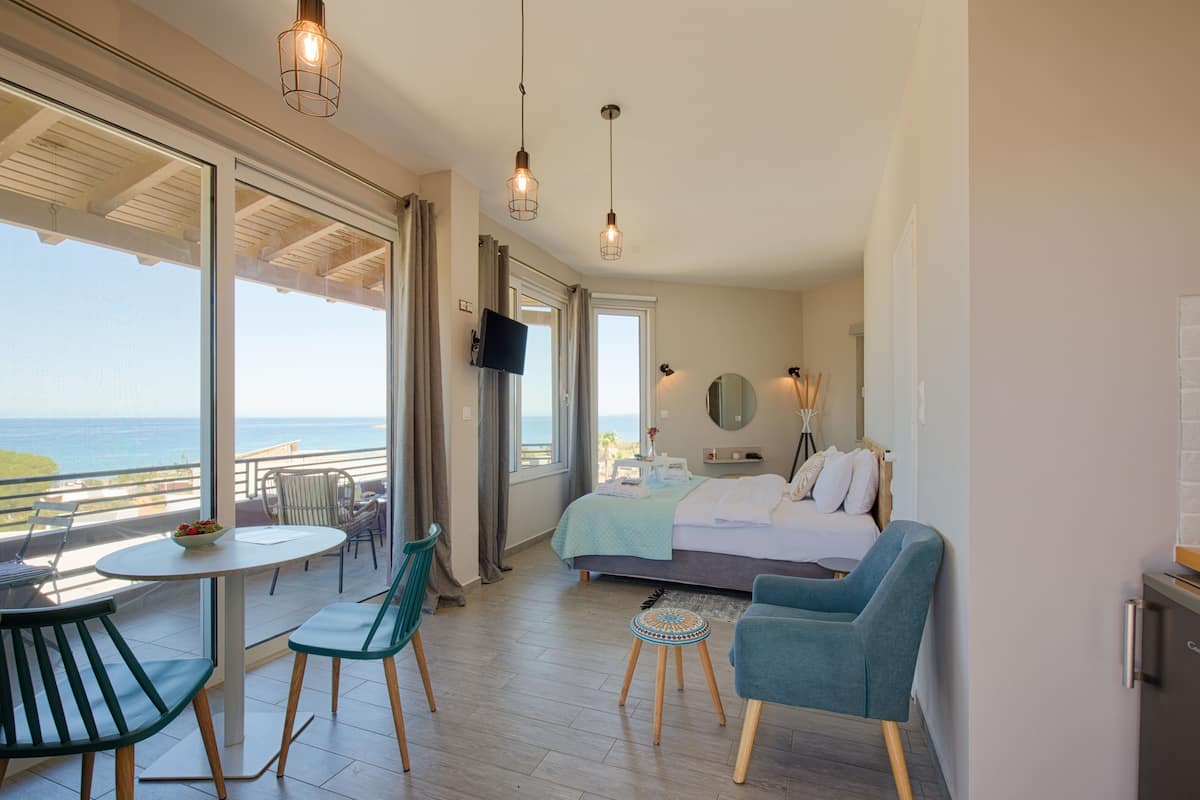 A hotel room with a balcony, a bed, a TV, and a dining area with chairs and a table.
