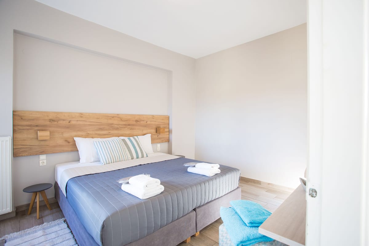A modern bedroom with a wooden headboard, a neatly made bed with blue bedding, and a blue towel on the floor.