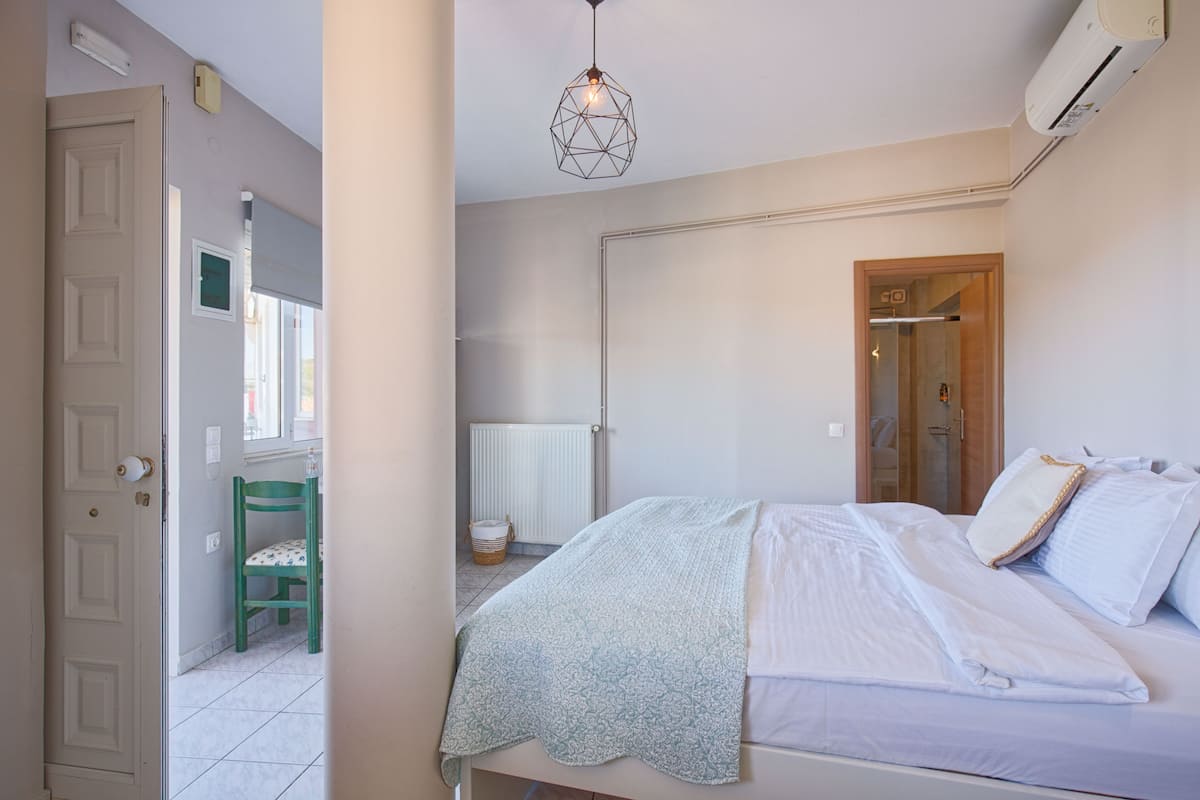 A bedroom with a bed, a green chair, a radiator, and a ceiling light fixture.