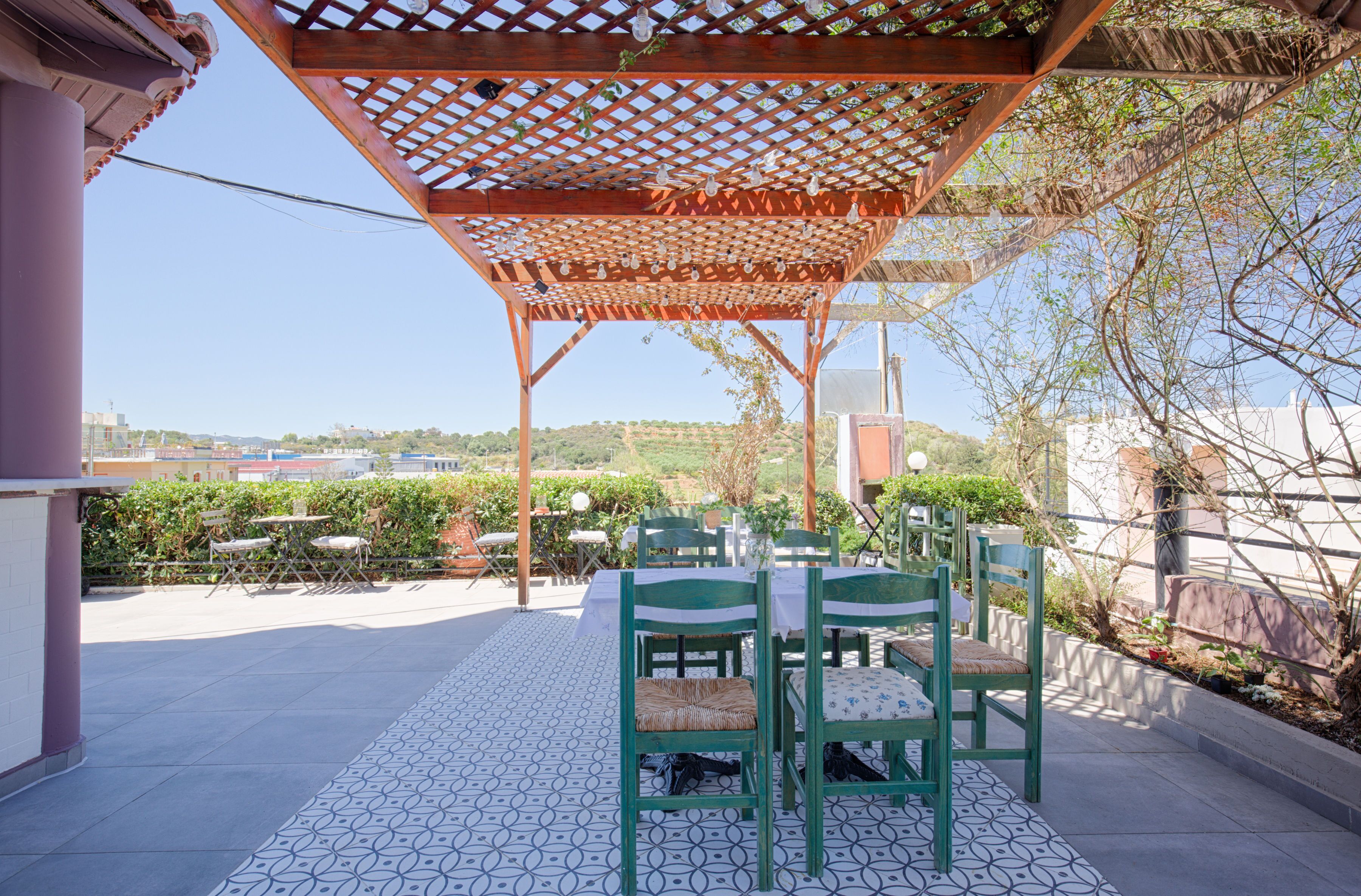 An outdoor patio with a pergola, green chairs, and a patterned floor.