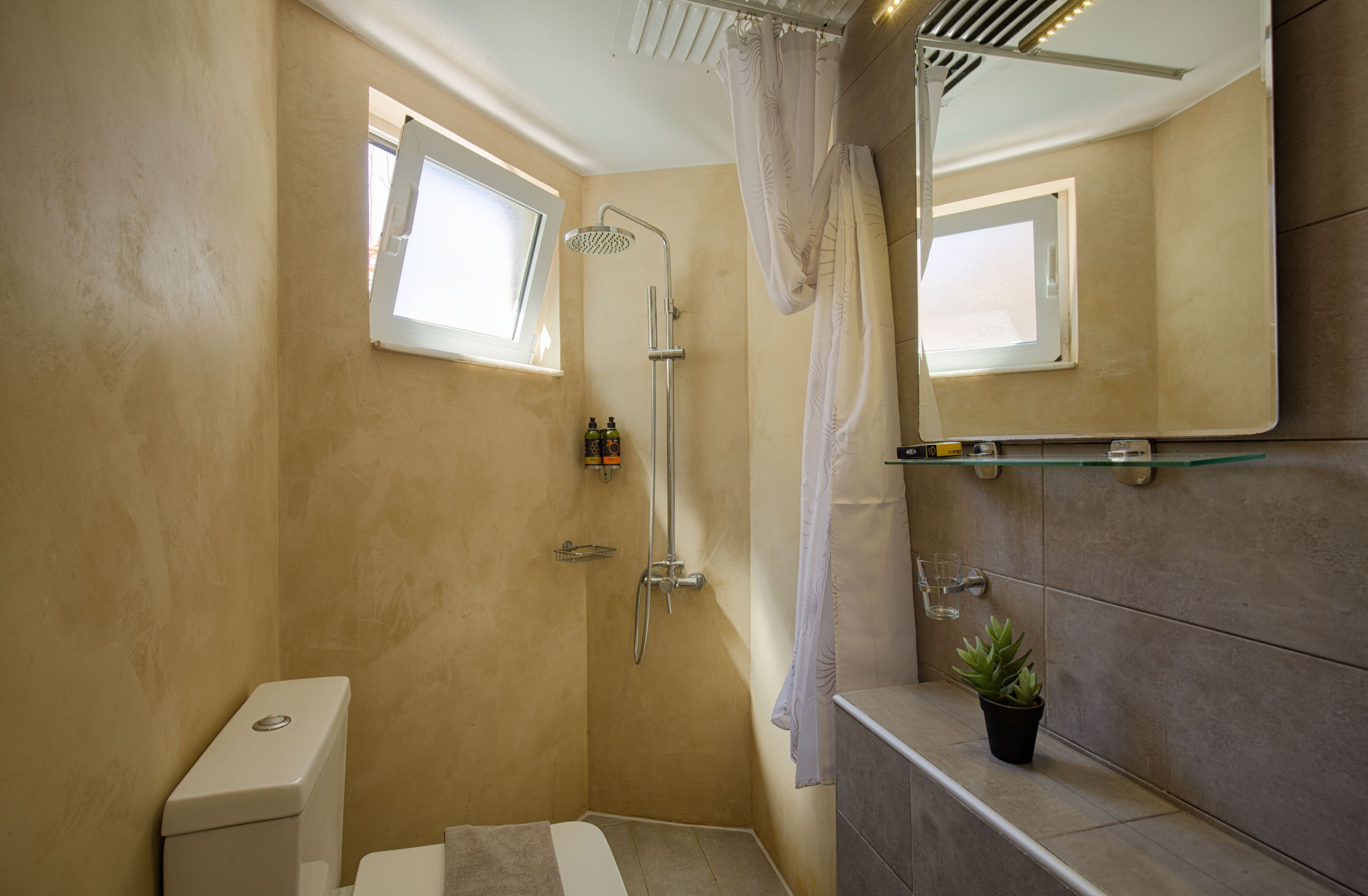 A compact bathroom with a shower, toilet, and a small window.