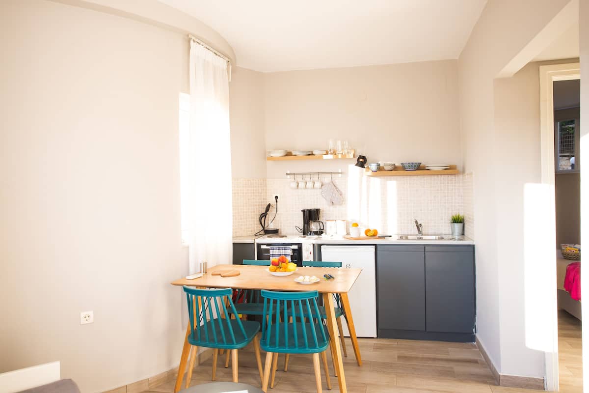 A compact kitchen with a dining area, featuring a wooden table, teal chairs, and a small island with a sink and countertop.