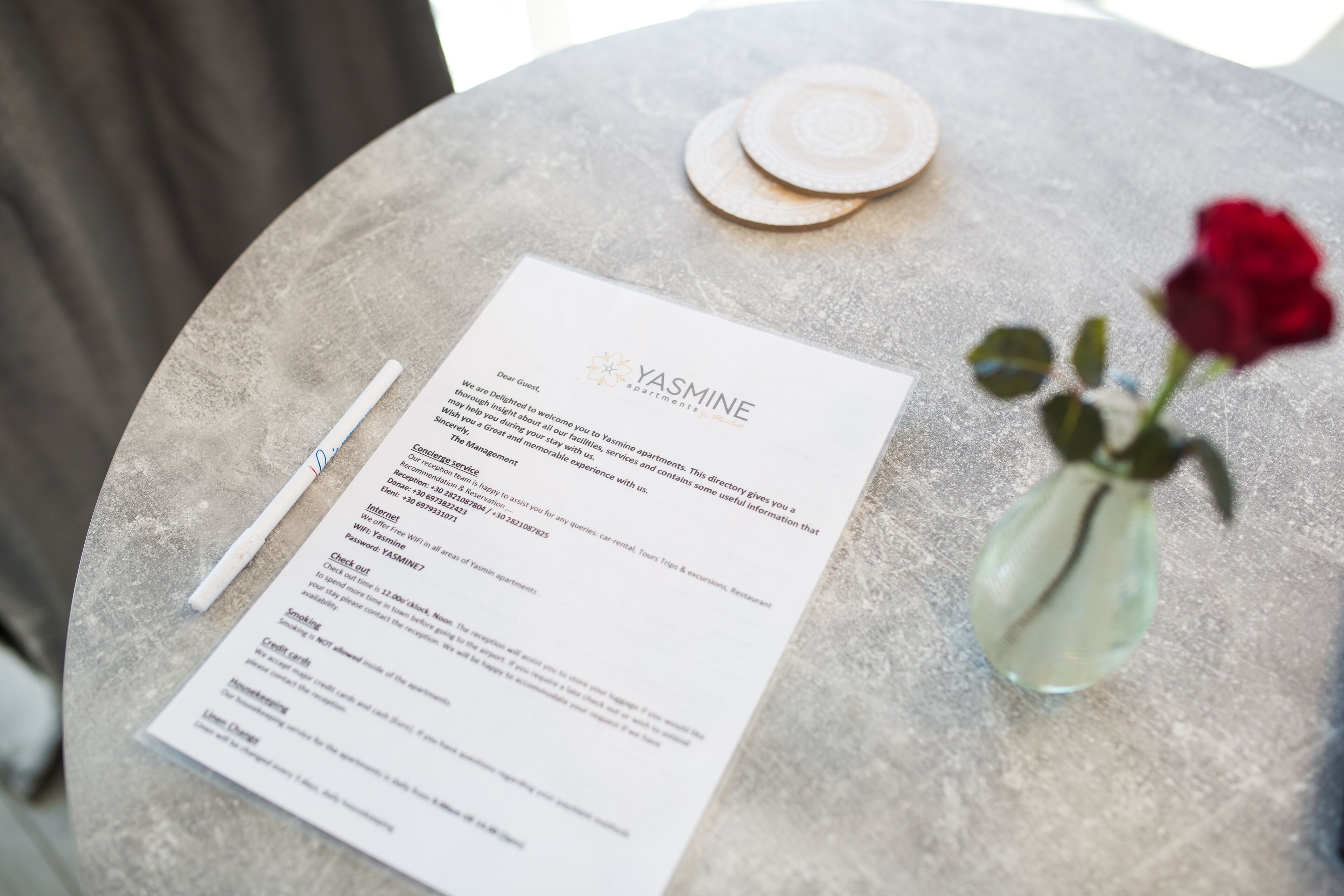 A welcome brochure titled 'Yasmine' on a stone table with a rose vase.
