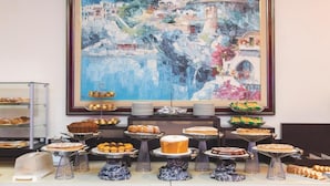 A buffet with various desserts and pastries, a large framed painting of a coastal scene, and a glass display case with baked goods. - Hotel Gabbiano (Mola di Bari)