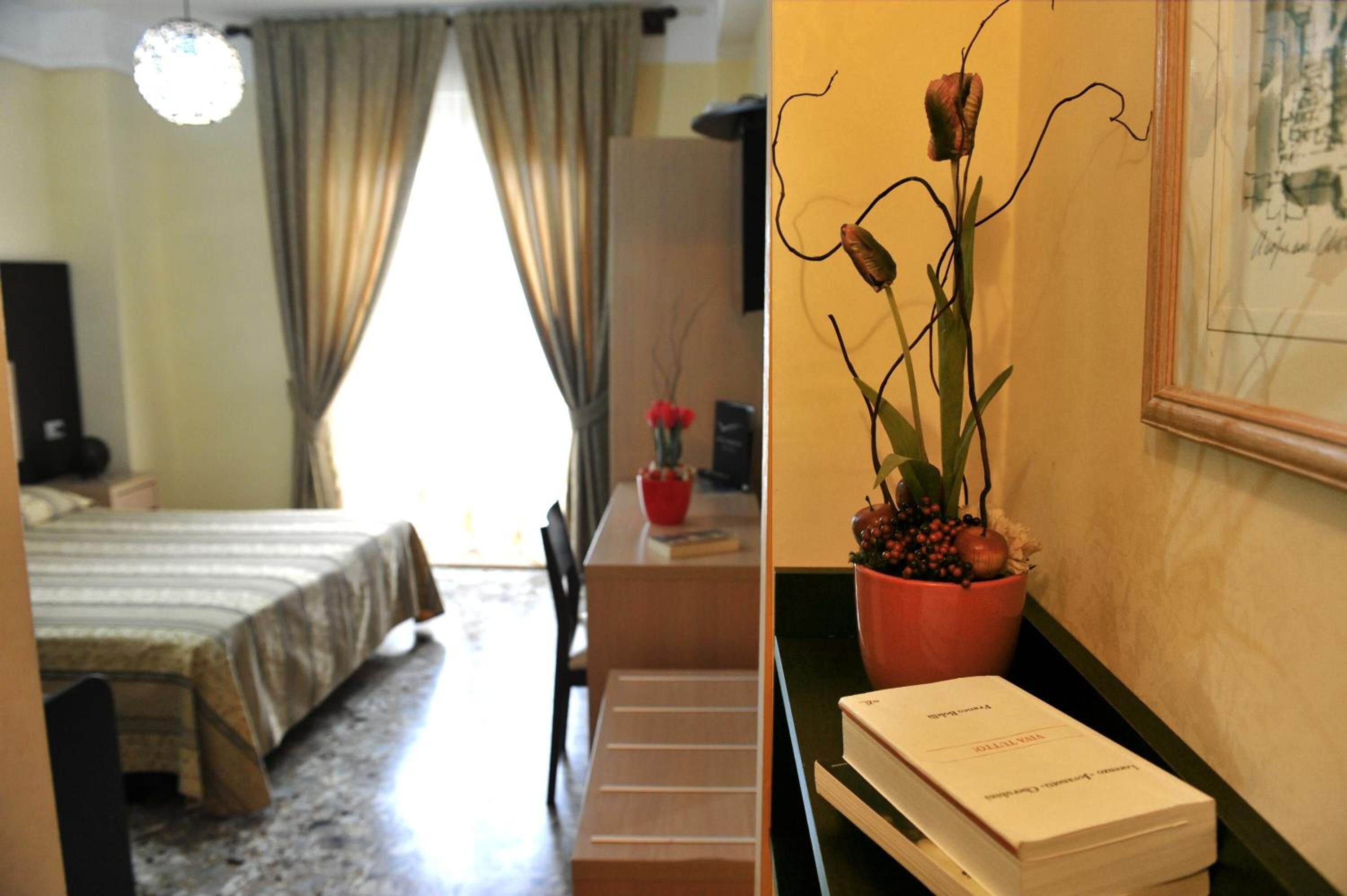 Una habitació d'hotel amb llit, escriptori, cadira, planta en test i quadre al mur.