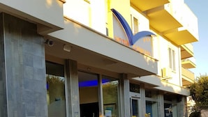 A hotel entrance with a modern design, featuring a glass facade, potted plants, and a tiled patio area. - Hotel Gabbiano (Mola di Bari)