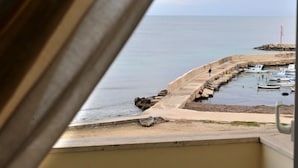 A view of a coastal area with boats docked at a pier, a sandy beach, and a rocky outcrop in the distance. - Hotel Gabbiano (Mola di Bari)