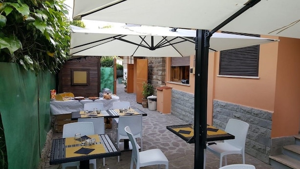 Une terrasse extérieure avec des tables et des chaises, un espace salon abrité et un mur en pierre.