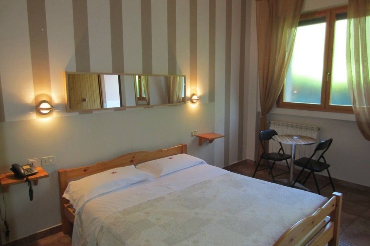 Een slaapkamer met een bed, nachtkastjes, een bureau met stoelen en een raam met gordijnen.